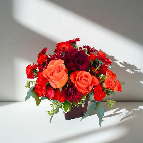 Bouquet of orange roses and red flowers in a dark vase