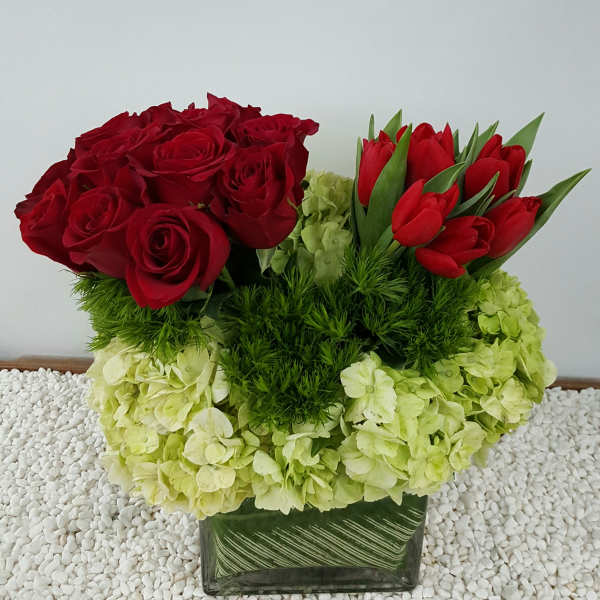 Red roses and red tulips arranged with pale green hydrangeas in a glass vase