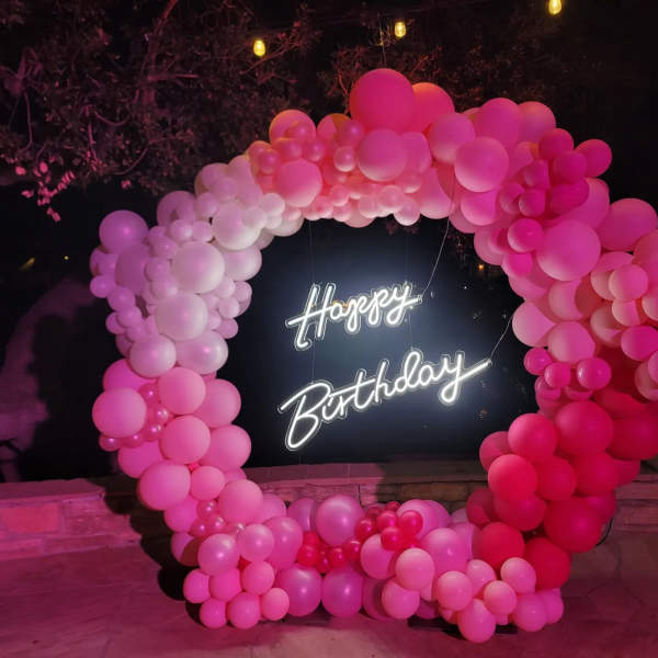 Pink balloon arch around a neon Happy Birthday sign
