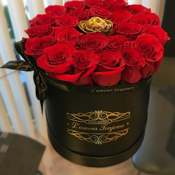 Red roses arranged in a black round box with a gold rose accent