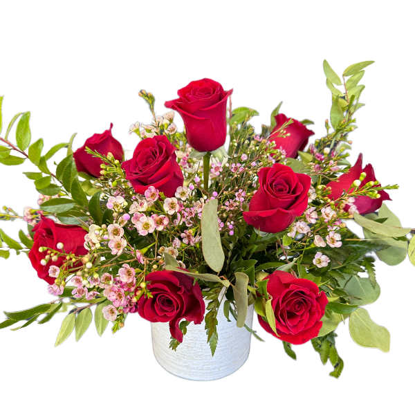 Red roses arranged in a white vase with small pink filler flowers