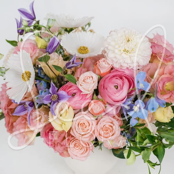 Pastel arrangement of pink and peach roses and ranunculus with white daisies in a white bowl vase