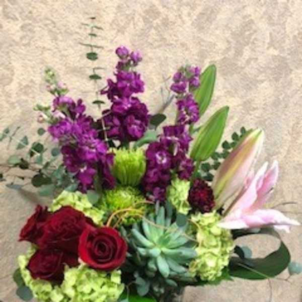 Bouquet of red roses, purple flowers, and lilies in a glass vase