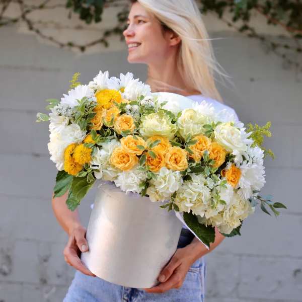 Woman holding a large white hatbox filled with yellow and white flowers