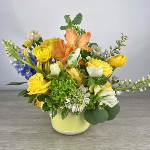 Colorful mixed bouquet in a yellow vase with orange, yellow, white, and blue flowers