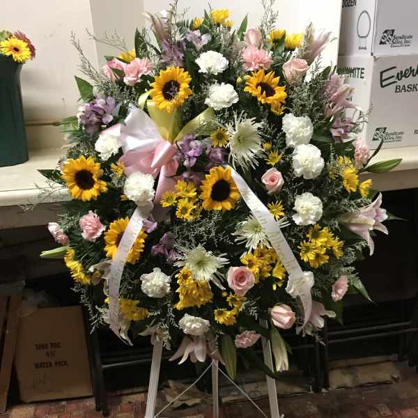 Large standing floral wreath with sunflowers, pink roses, and white blooms on an easel