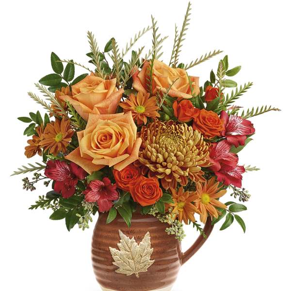 Orange roses and chrysanthemums in a brown leaf-accented pitcher vase