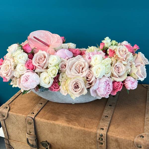 Low floral arrangement of pale pink and white roses with anthurium in a gray container