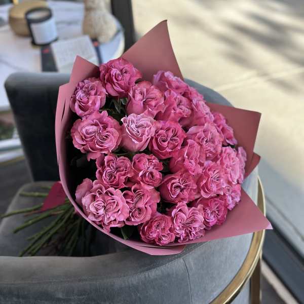 Large bouquet of bright pink roses wrapped in pink paper resting on a gray chair