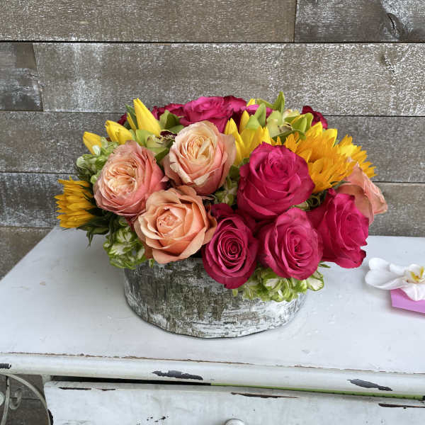Mixed roses and sunflowers arranged in a rustic round container