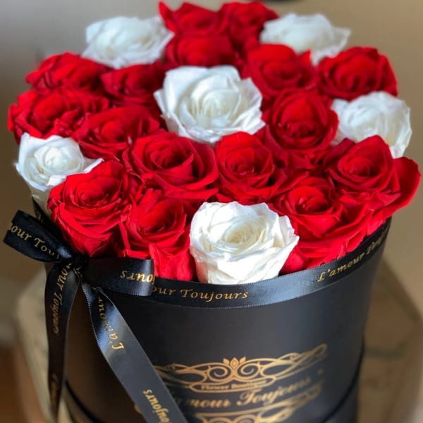 Red and white roses arranged in a black round box with a ribbon bow