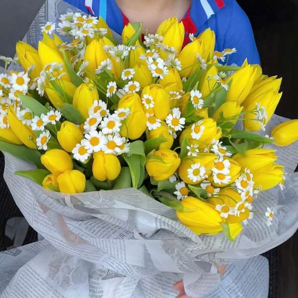 Bouquet of yellow tulips and small white daisies wrapped in paper