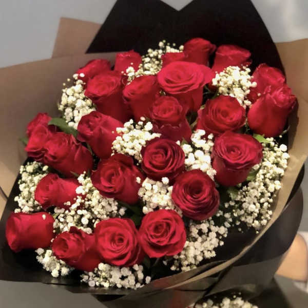 Hand-tied bouquet of red roses with white filler flowers wrapped in black and kraft paper