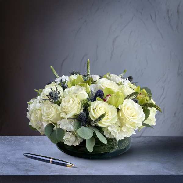 Low round arrangement of white roses and hydrangeas in a dark green bowl