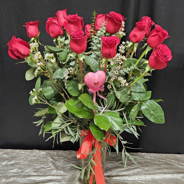 Bouquet of red roses with greenery in a clear glass vase and pink heart pick