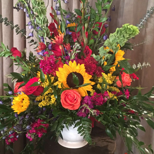 Tall mixed flower arrangement in a white vase with sunflowers and roses