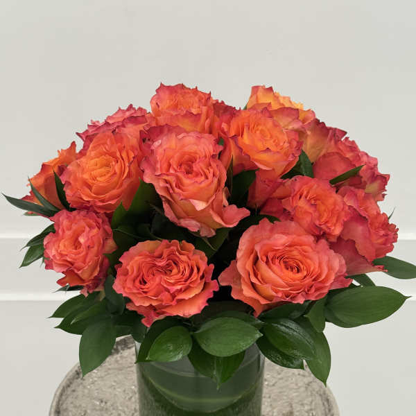 Orange roses arranged in a glass vase with dark green foliage
