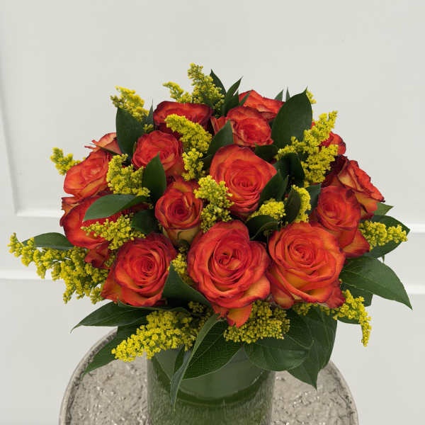 Bouquet of red-orange roses in a glass vase with yellow filler flowers