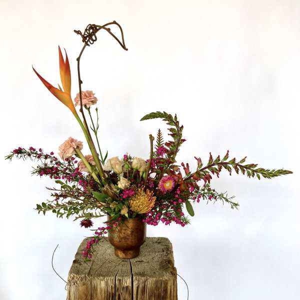 Tropical floral arrangement in a copper vase with orange bird-of-paradise and pink blooms