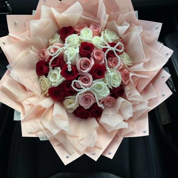 Bouquet of red, pink, and white roses wrapped in blush paper with pearl accents