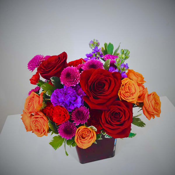 Bouquet of red and orange roses with purple and pink flowers in a dark vase