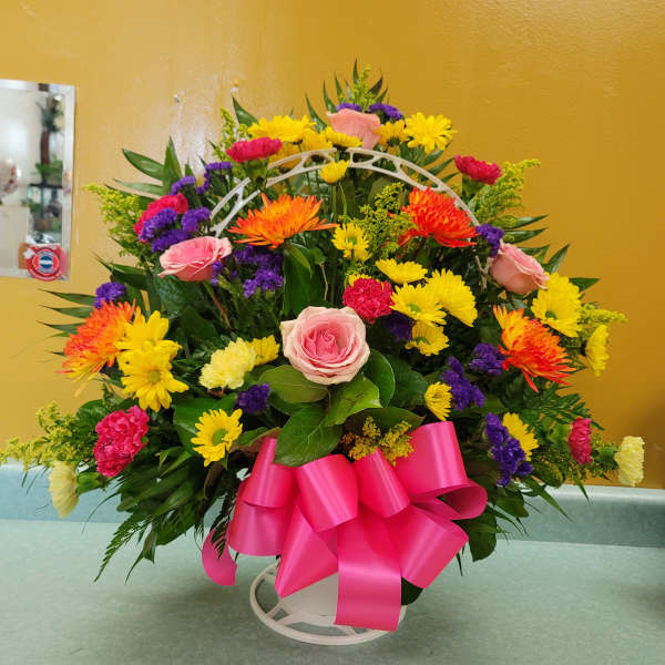 Colorful mixed flower arrangement with a pink ribbon on a white stand