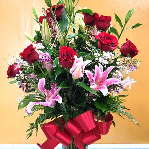 Red roses and pink lilies in a clear glass vase with a red ribbon