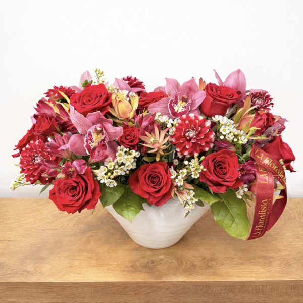Red roses and pink orchids arranged in a white bowl vase