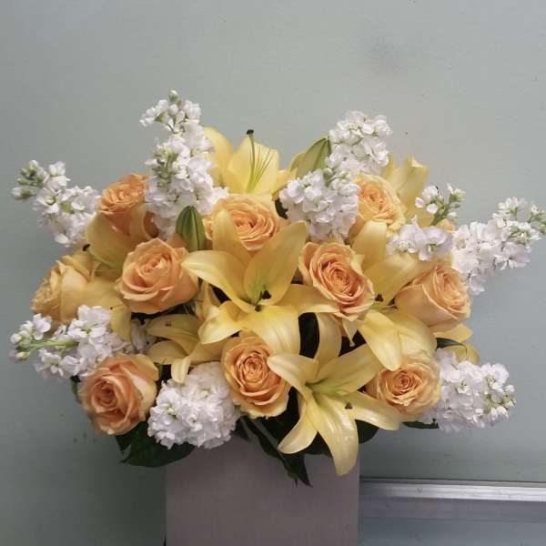 Bouquet of yellow lilies, peach roses, and white blossoms in a box
