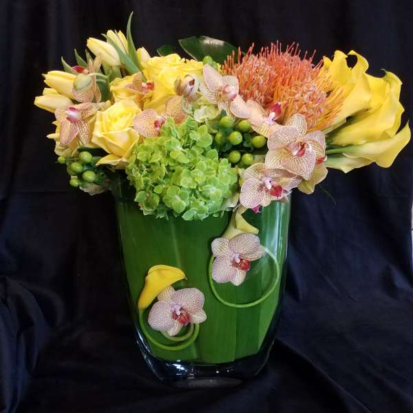 Yellow flowers and orchids arranged in a green glass vase