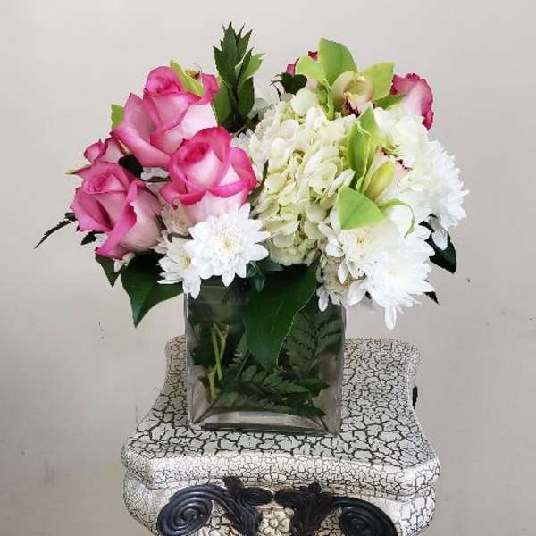 Pink roses and white flowers arranged in a square glass vase