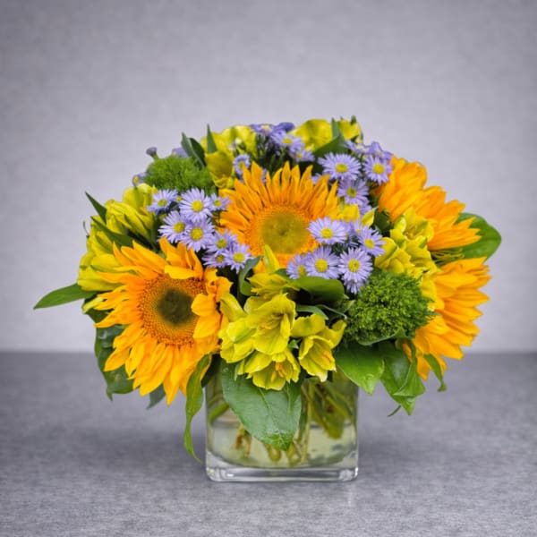 Bouquet of yellow sunflowers and purple daisies in a glass vase