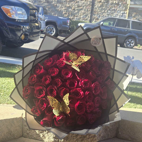 Large bouquet of red roses wrapped in black and white paper with gold butterfly accents