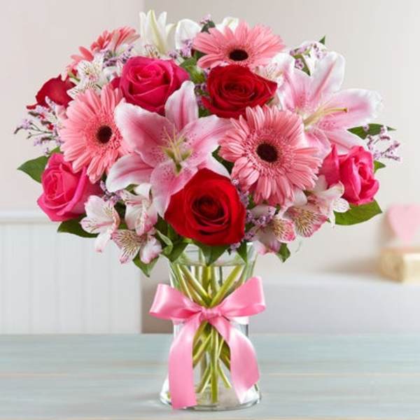 Bouquet of pink and red flowers in a glass vase with a pink ribbon