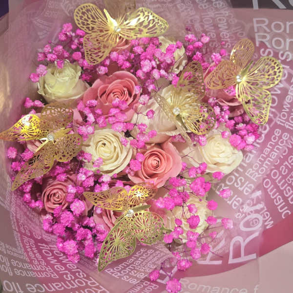 Bouquet of pink and cream roses with bright pink filler and gold butterfly decorations