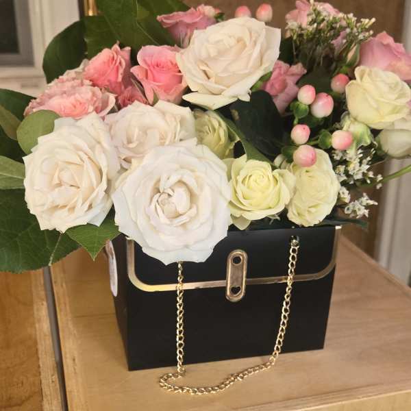 Pink and white roses arranged in a black handbag-style box