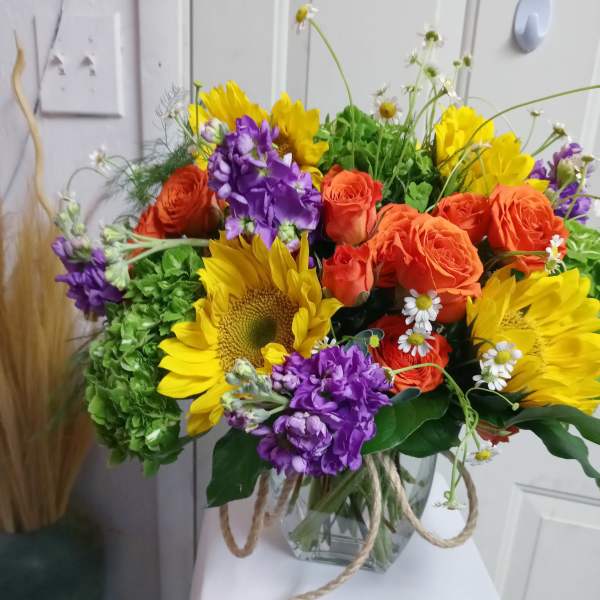 Bouquet of sunflowers, orange roses, and purple flowers in a glass vase