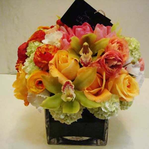 Cymbidium orchids, roses, ranunculus, tulips, and hydrangea in a square vase.