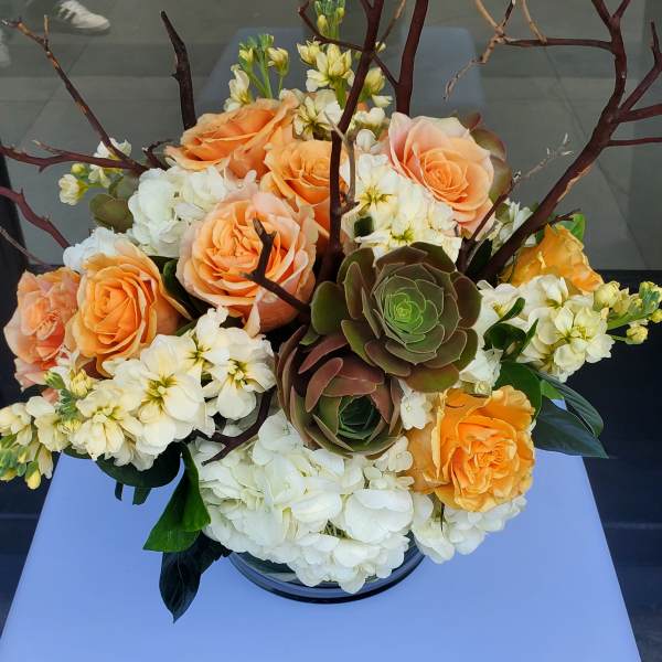 Peach roses, white hydrangeas, succulents, and branches arranged in a low glass vase.