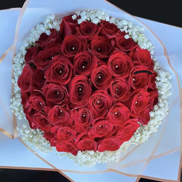 Round bouquet of red roses with pearl centers, edged with small white flowers in white wrapping.