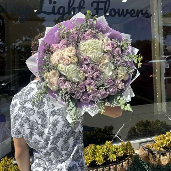 Large bouquet of lavender and cream roses wrapped in purple paper