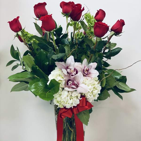 Red roses and pale orchids in a clear glass vase with a red ribbon