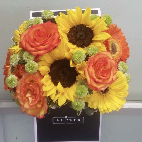 Bouquet of sunflowers, orange roses, and green button mums in a black box