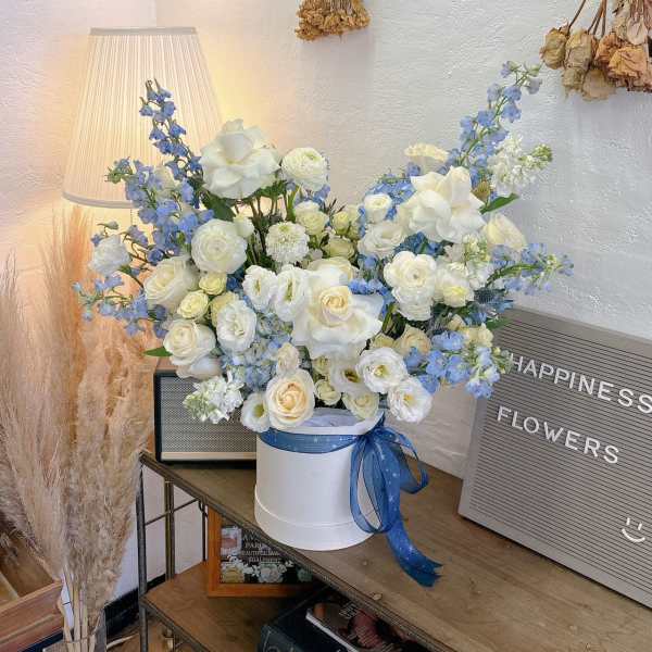 White and blue flower arrangement in a round box with a ribbon