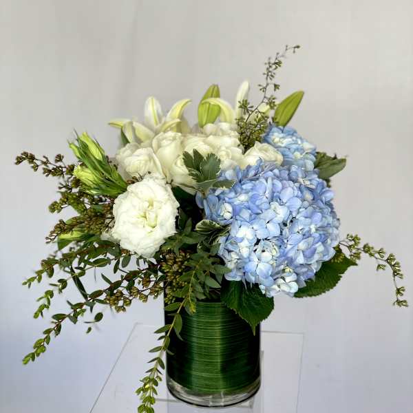 Blue hydrangeas and white lilies in a green glass vase