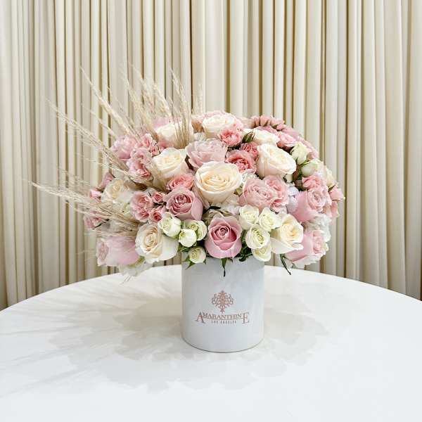 Round arrangement of blush, pink, and cream roses in a white hatbox-style container