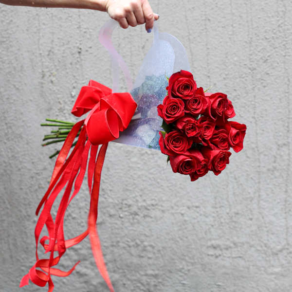 Handheld bouquet of red roses wrapped in sheer plastic with a red ribbon
