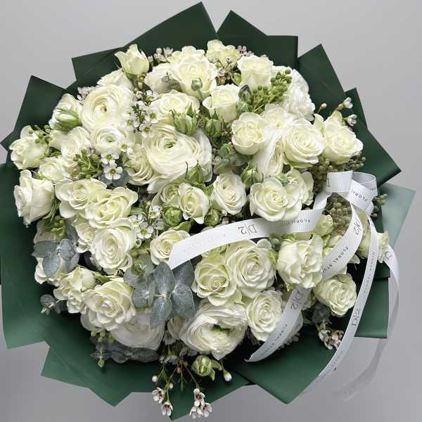 Bouquet of white roses and ranunculus wrapped in dark green paper