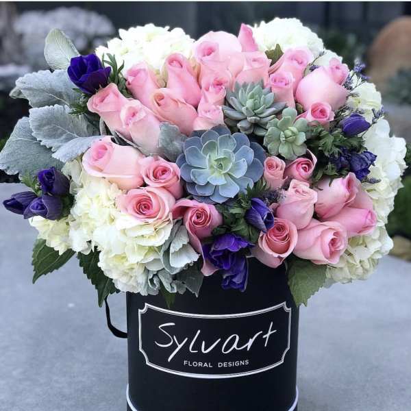 Pink roses, white hydrangeas, and purple blooms in a black hatbox