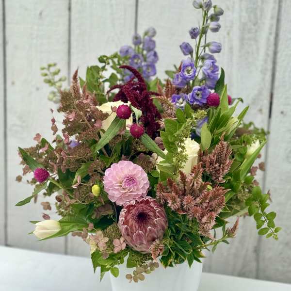 Mixed bouquet of pink, purple, and cream flowers in a white vase
